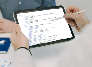 Eine Hand hält einen Tablet-Computer. Auf dem Bildschirm sind technische Code-Zeilen zu sehen, die die Transformation von Richtlinien in Smarte Standards darstellen.