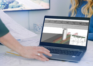 Ein Laptop steht auf einem Schreibtisch. Auf dem aufgeklappten Bildschirm ist ein BIM-Modell zu erkennen. Im Vordergrund ist die Hand einer Bearbeiterin zu sehen, die mit dem Touchpad navigiert.